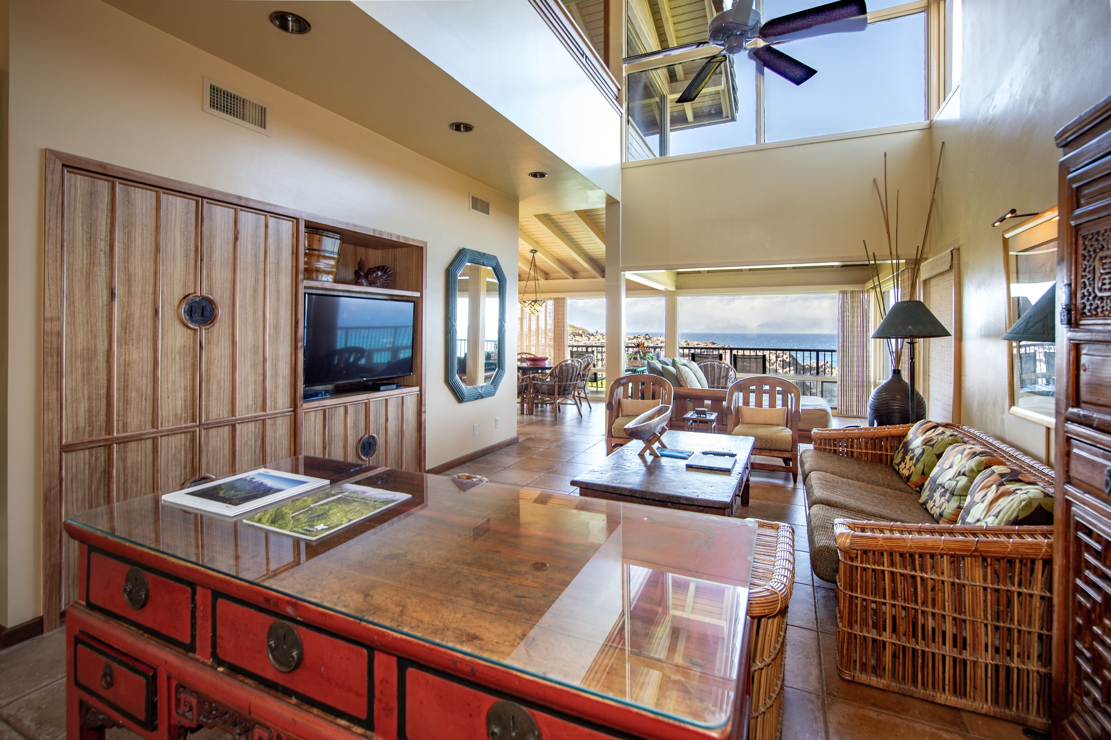 A spacious living area with a large glass coffee table, wicker furniture, a television, and a view of the ocean.