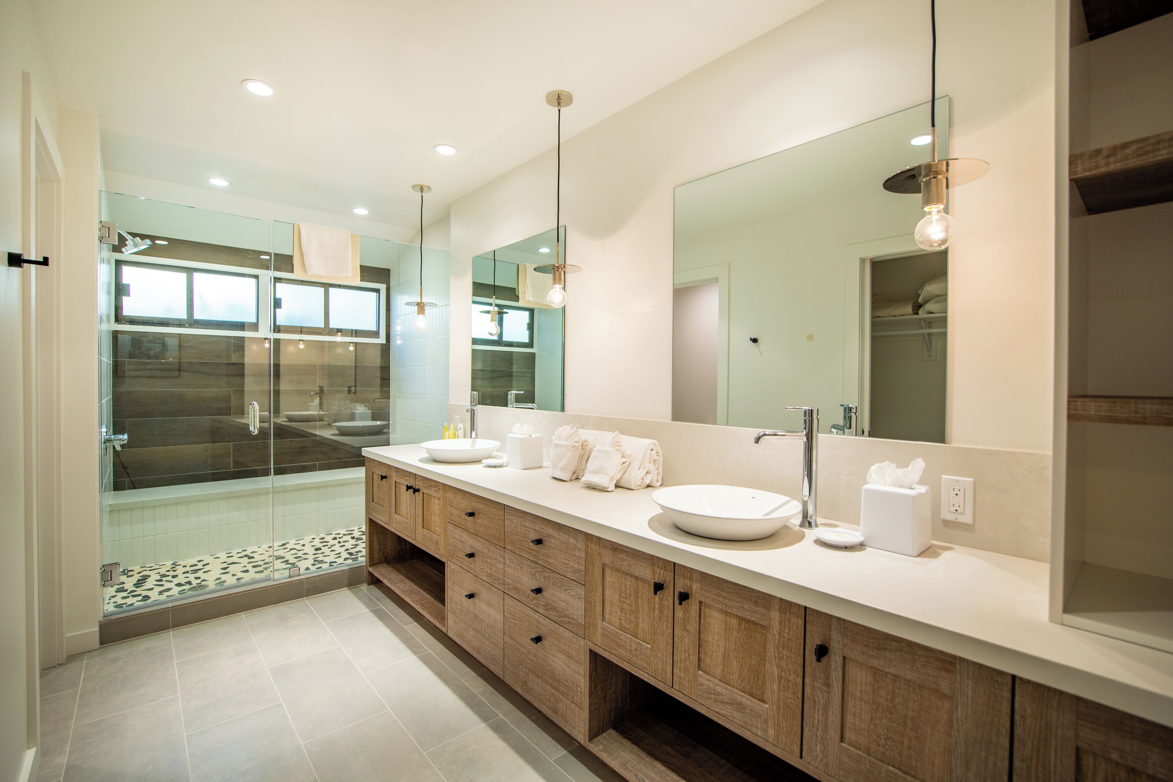 A modern bathroom with a glass shower enclosure, a large mirror, and a wooden vanity with drawers.