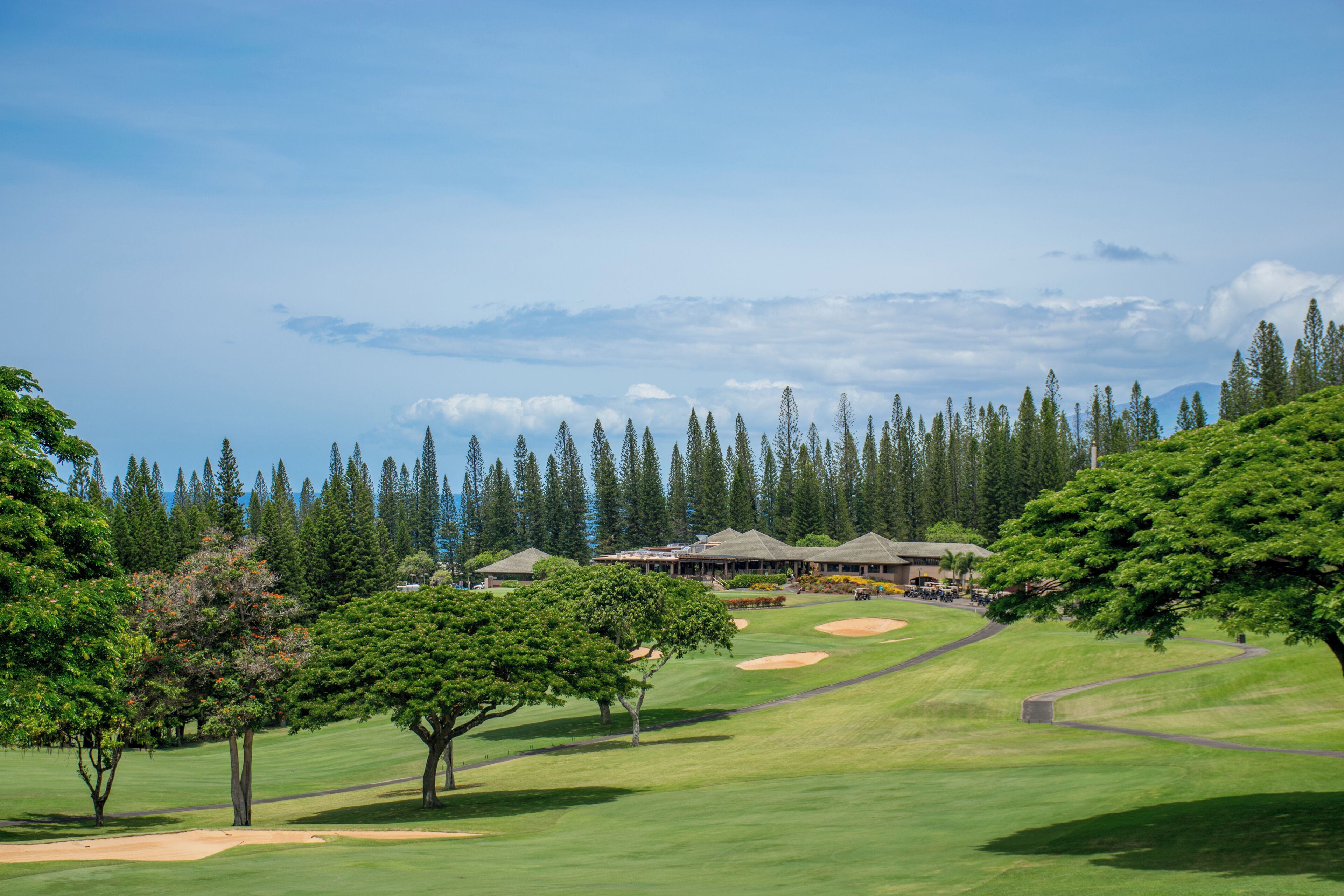 A golf course with a clubhouse, surrounded by trees and a clear sky.