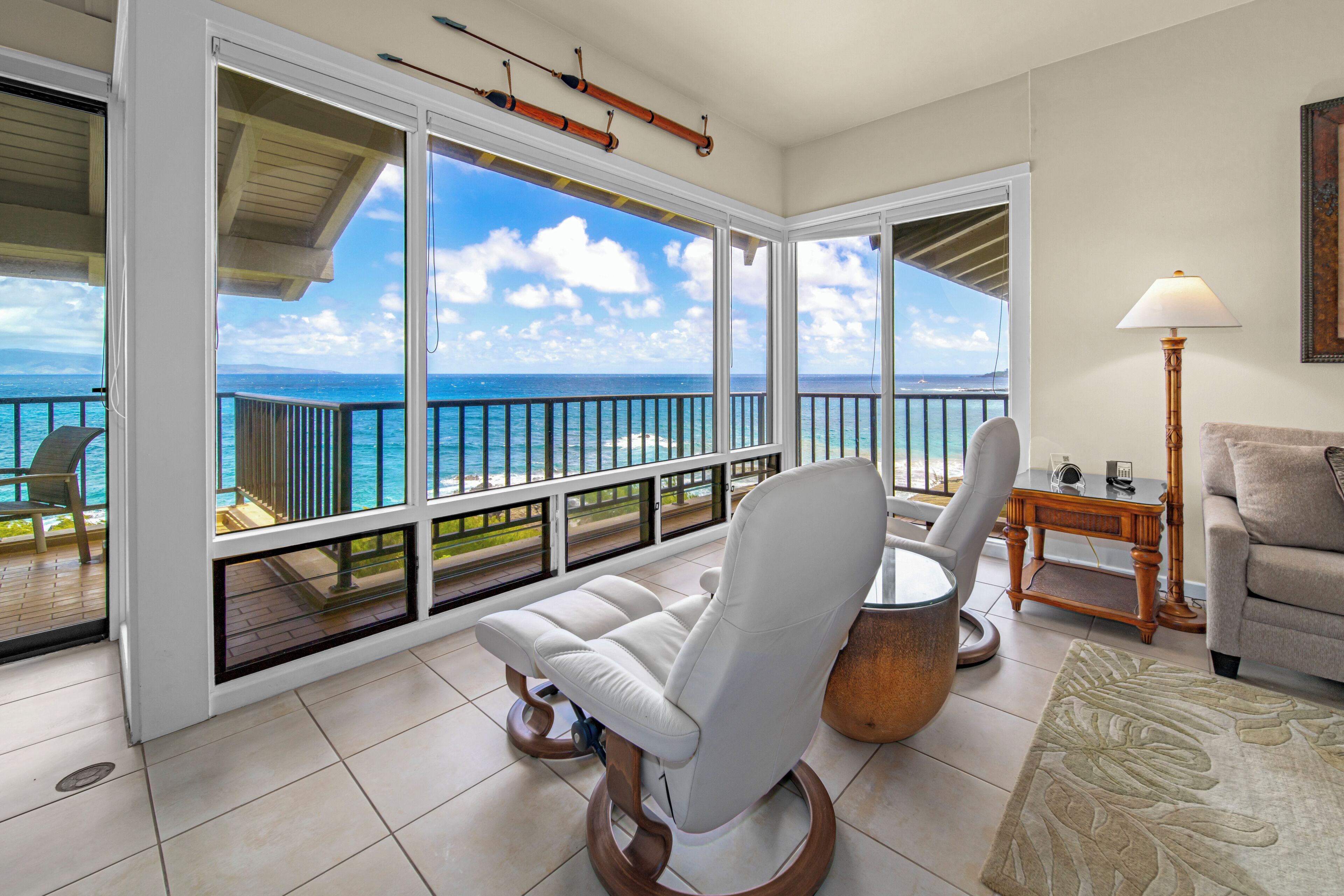 A room with a view of the ocean, a white chair, a small table, and a lamp.