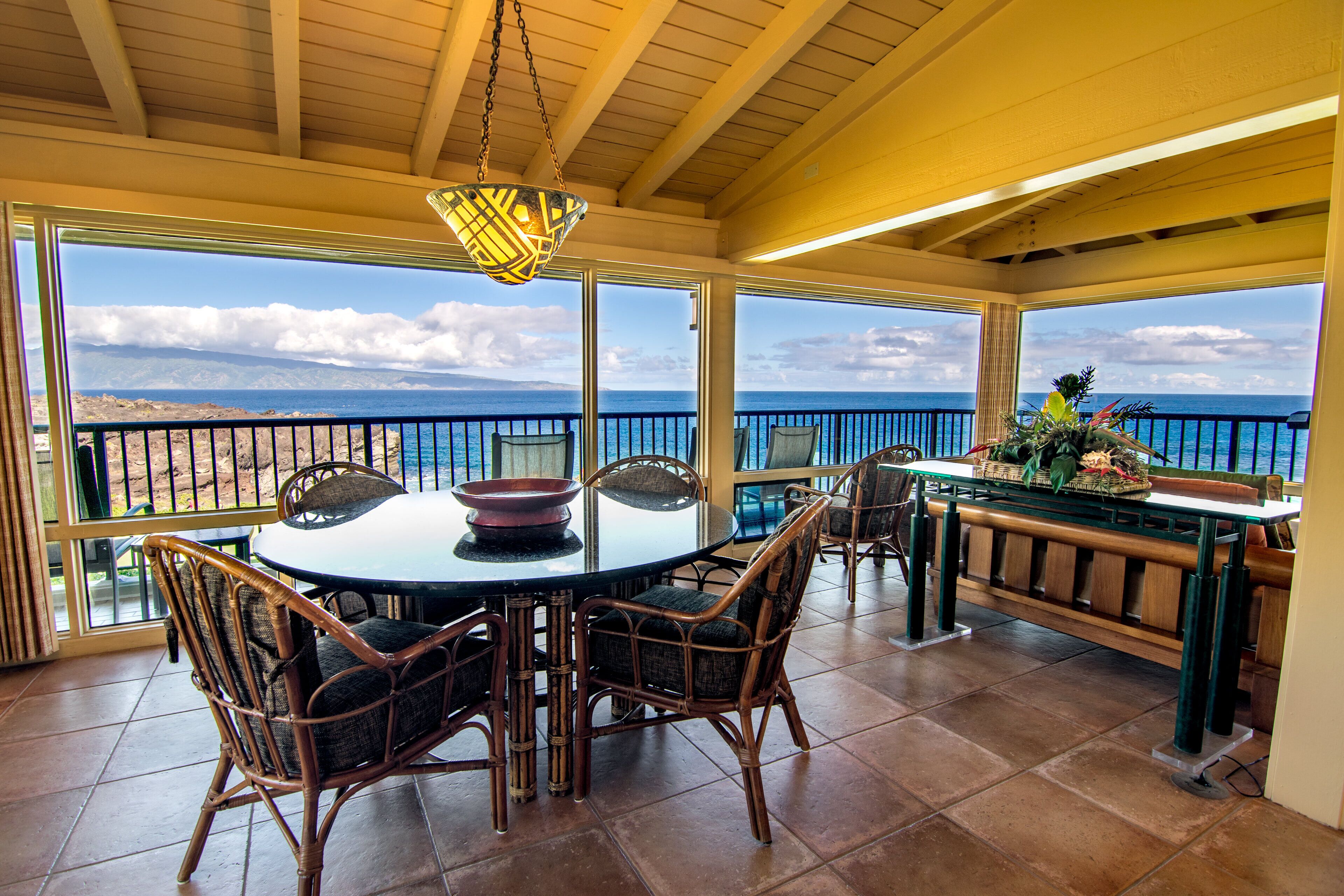 A dining area with a round table, wicker chairs, and a view of the ocean.