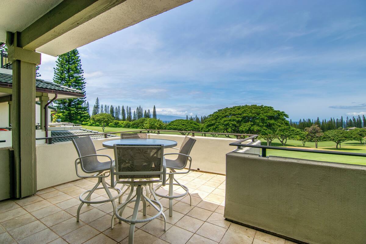 Ein Balkon mit Tisch und Stühlen, mit Blick auf einen Golfplatz und Bäume.