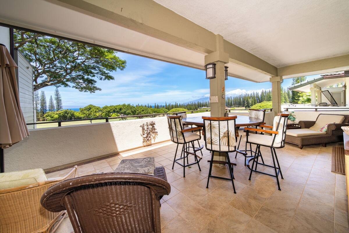 Eine überdachte Terrasse mit Korbmöbeln, einem Esstisch und Blick auf eine üppige Landschaft.