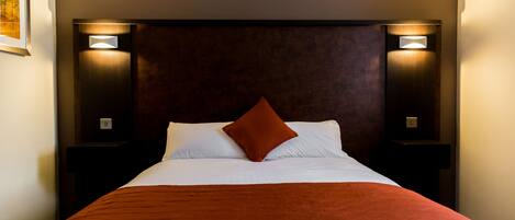 A hotel room with a large bed, a brown headboard, and two wall-mounted nightstands.