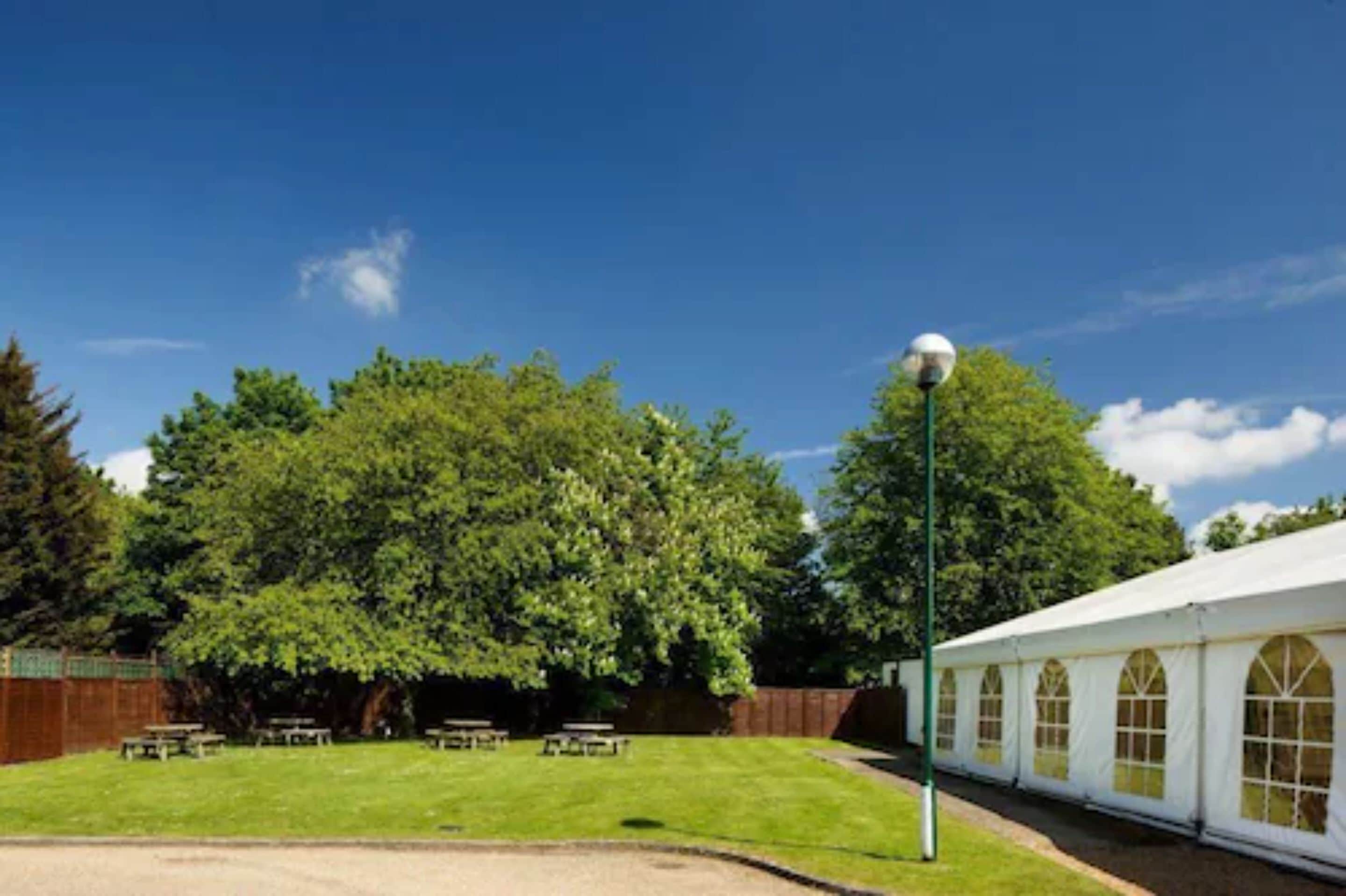 A tented outdoor area with tables and chairs, surrounded by trees and a clear sky.
