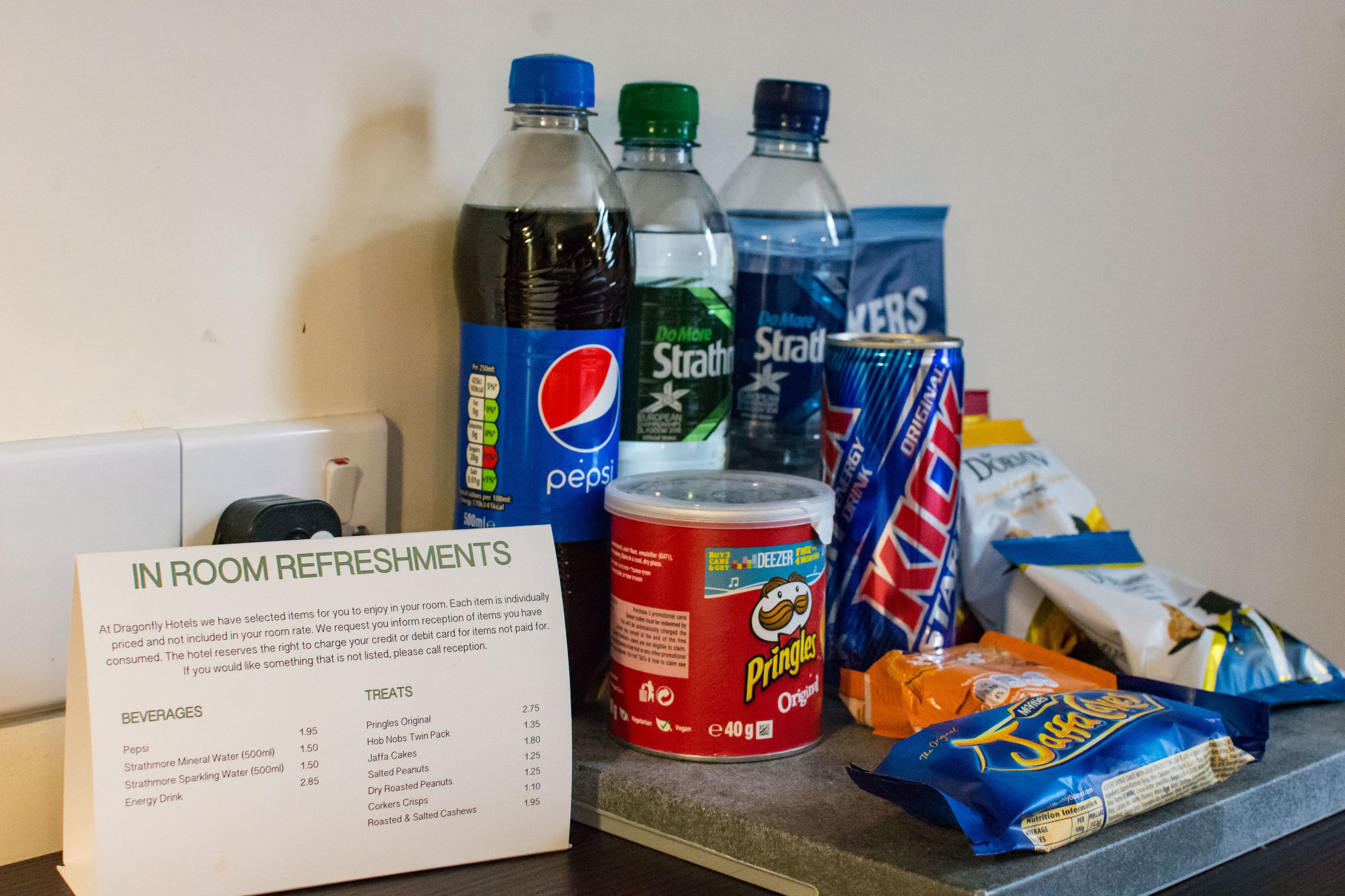 Una mesa con un menú que enumera bebidas y aperitivos, incluyendo Pepsi, Agua Mineral Strathmore y Pringles.