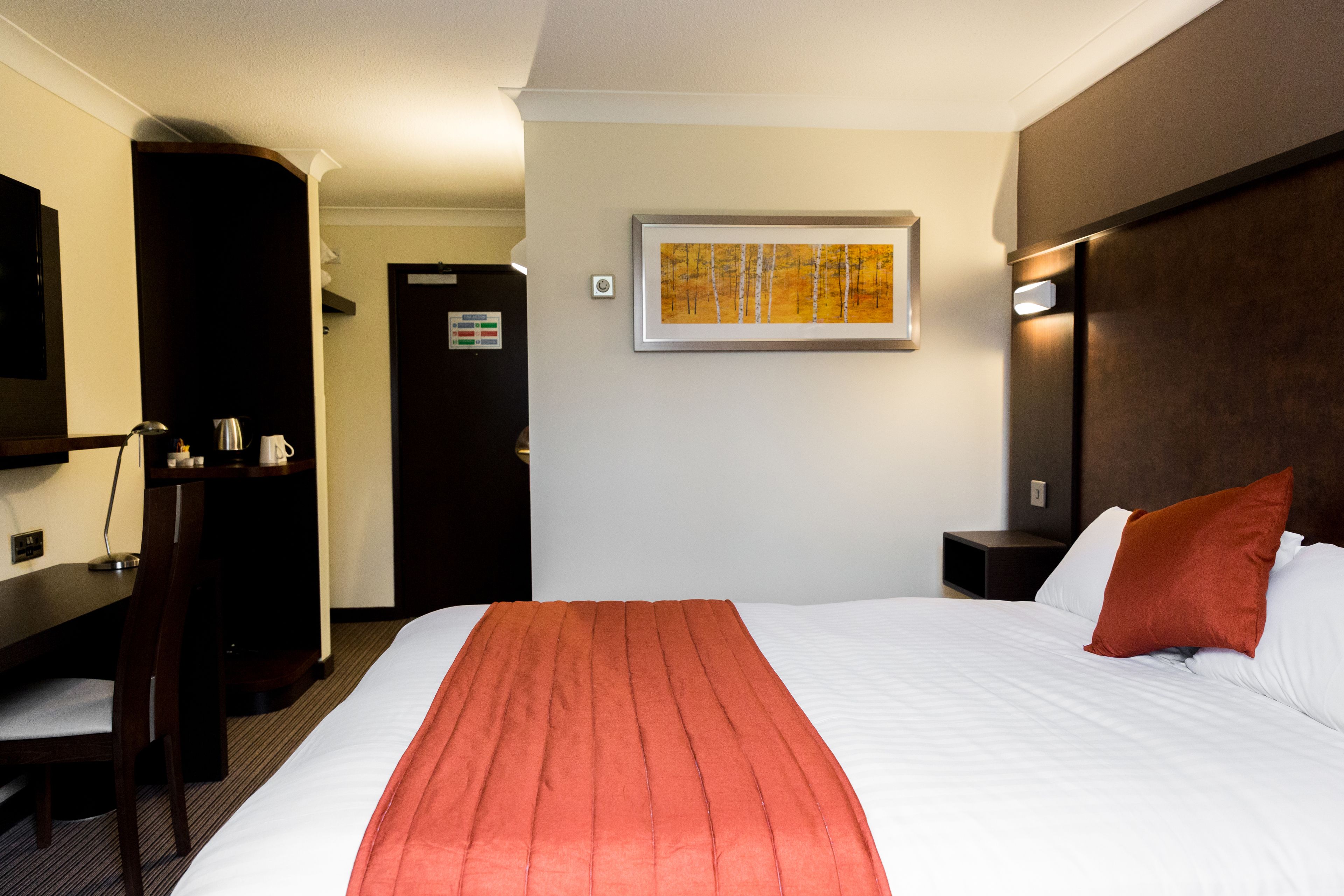 Hotellihuone, jossa on suuri sänky, työpöytä tuolilla, televisio ja taulu seinällä.