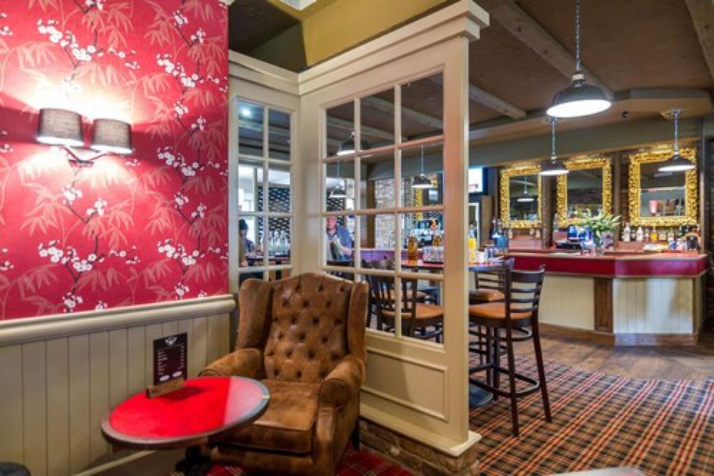 A bar area with a red floral wallpaper, a tufted leather armchair, and a bar counter with stools.