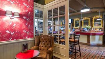 A bar area with a red floral wallpaper, a tufted leather armchair, and a bar counter with stools.