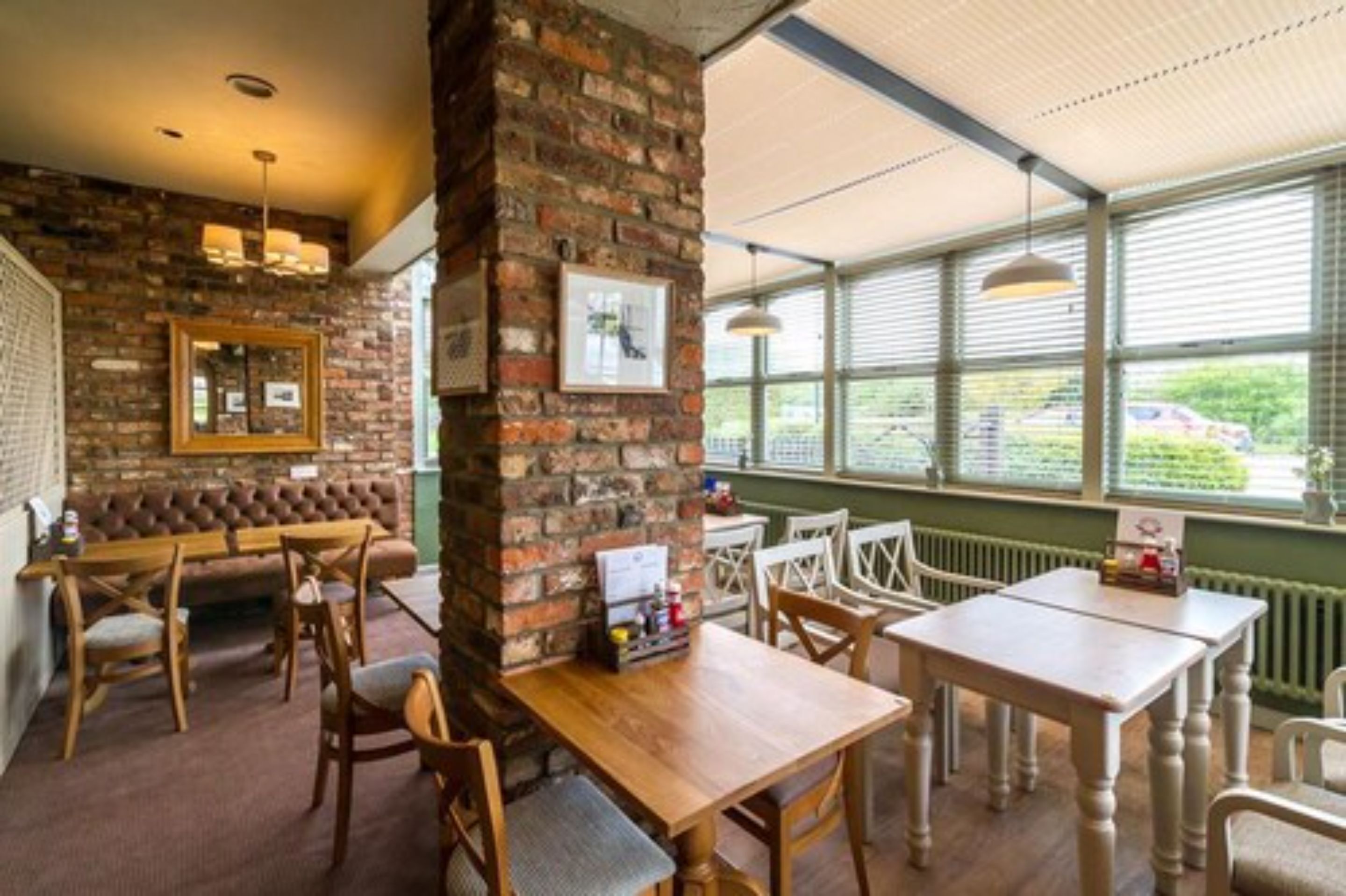 A cozy restaurant with brick walls, wooden furniture, and large windows offering a view of the outside.