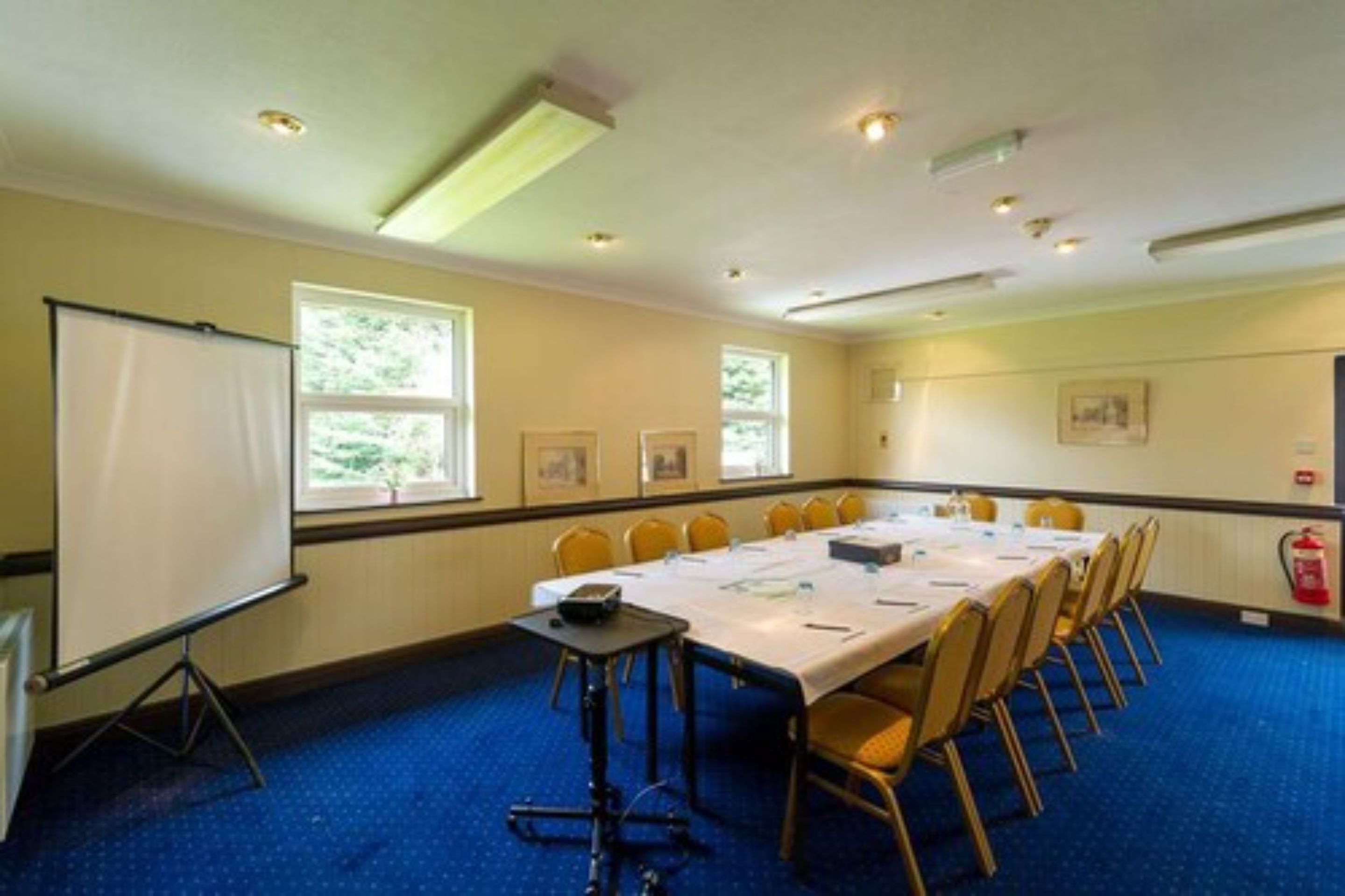 A conference room with a long table, chairs, a projector screen, and windows.