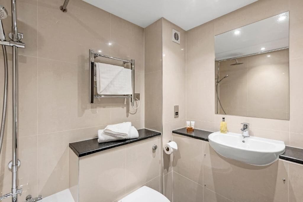 A modern bathroom with a shower, toilet, sink, and a large mirror.