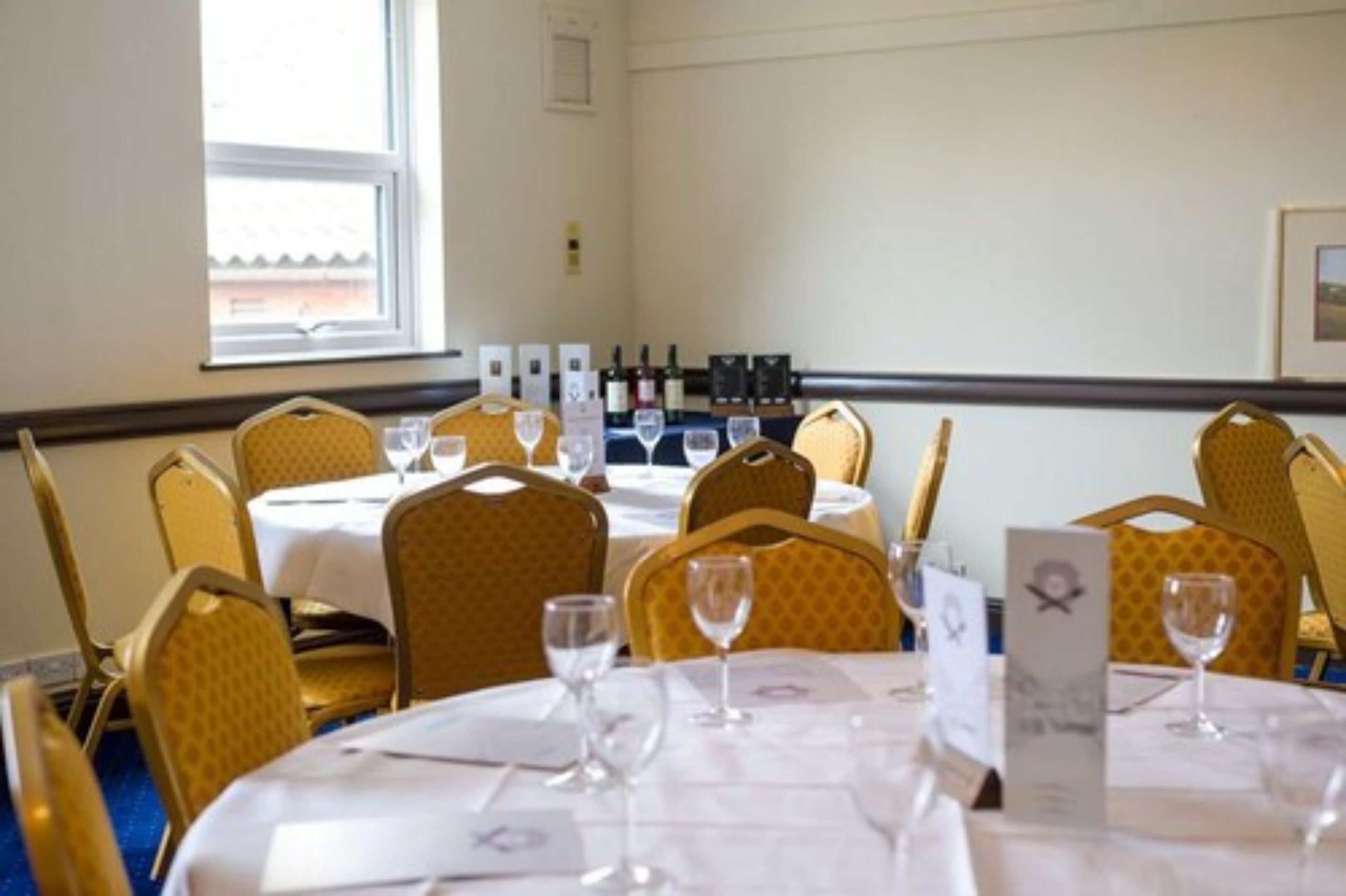 A dining area with tables set for service, chairs, and wine glasses.
