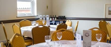 Un comedor con mesas dispuestas para el servicio, sillas y copas de vino.