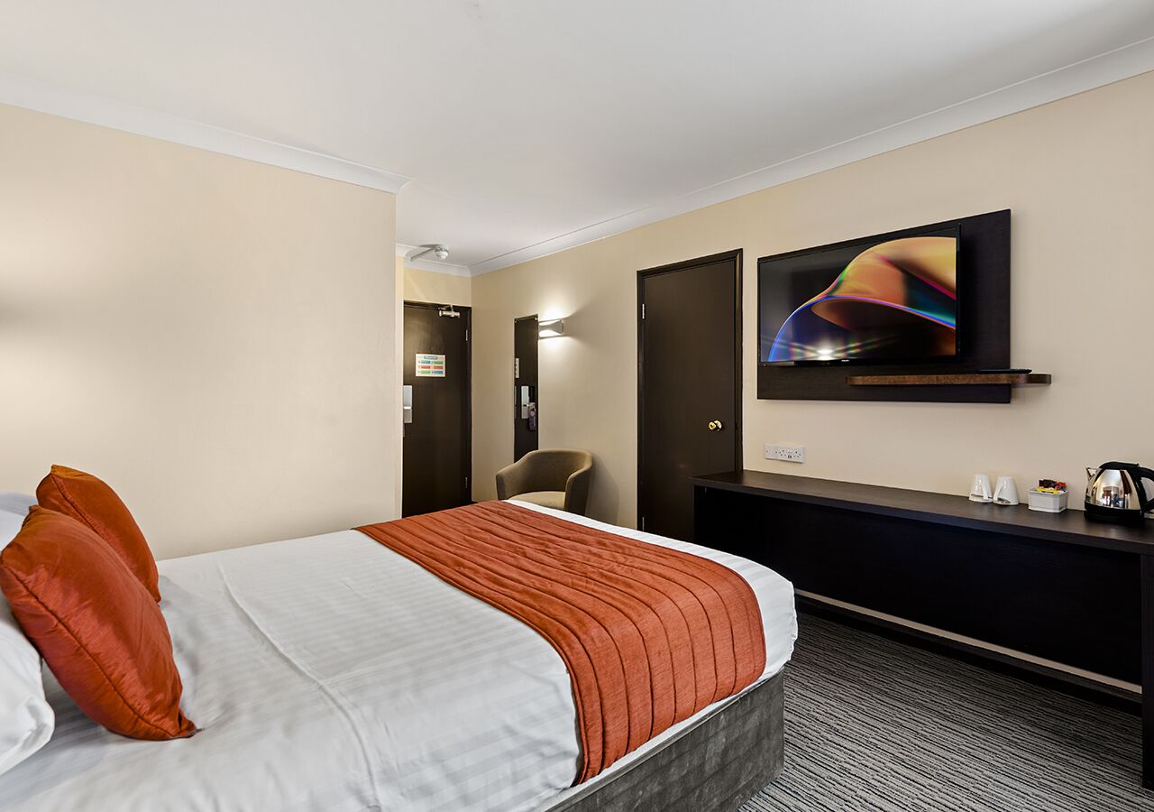 A hotel room with a bed, a desk, a television, and a door.