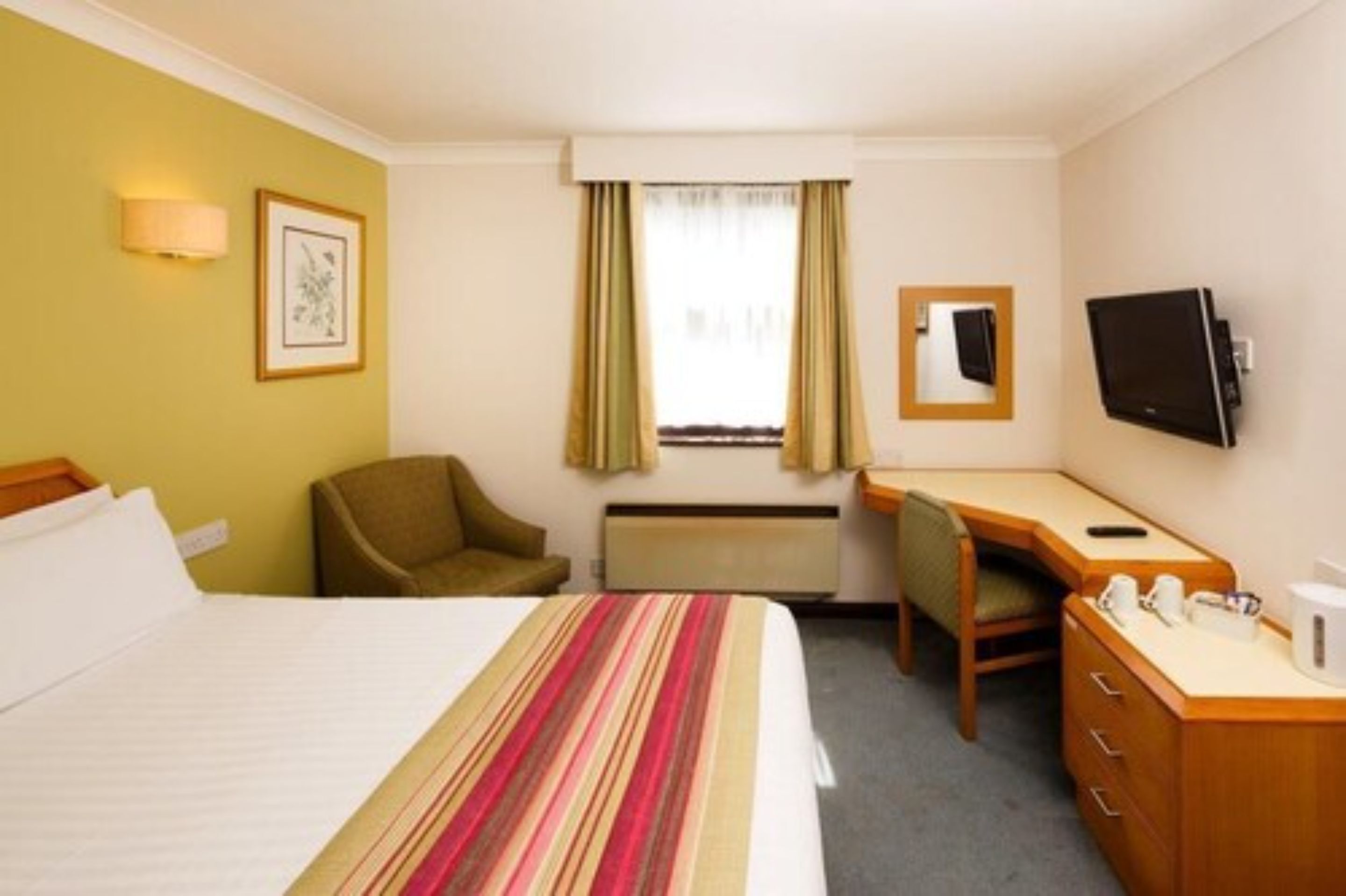 Une chambre d’hôtel avec un lit, un bureau, une chaise, une télévision et une fenêtre avec des rideaux.