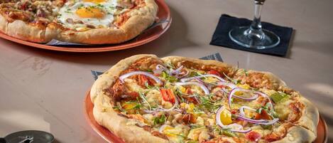 Dos pizzas sobre platos con una copa de vino en una mesa.