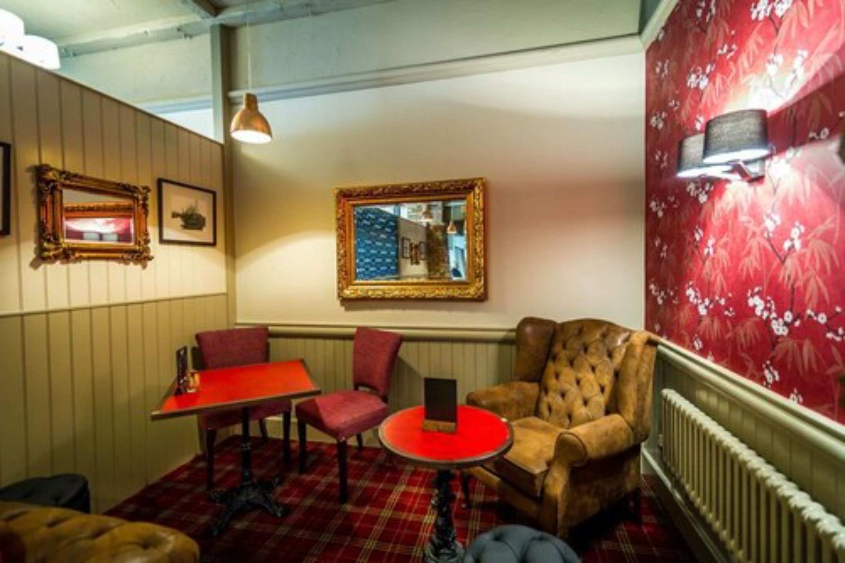 A room with a red table, two chairs, a red rug, a tufted armchair, a mirror, and a radiator.