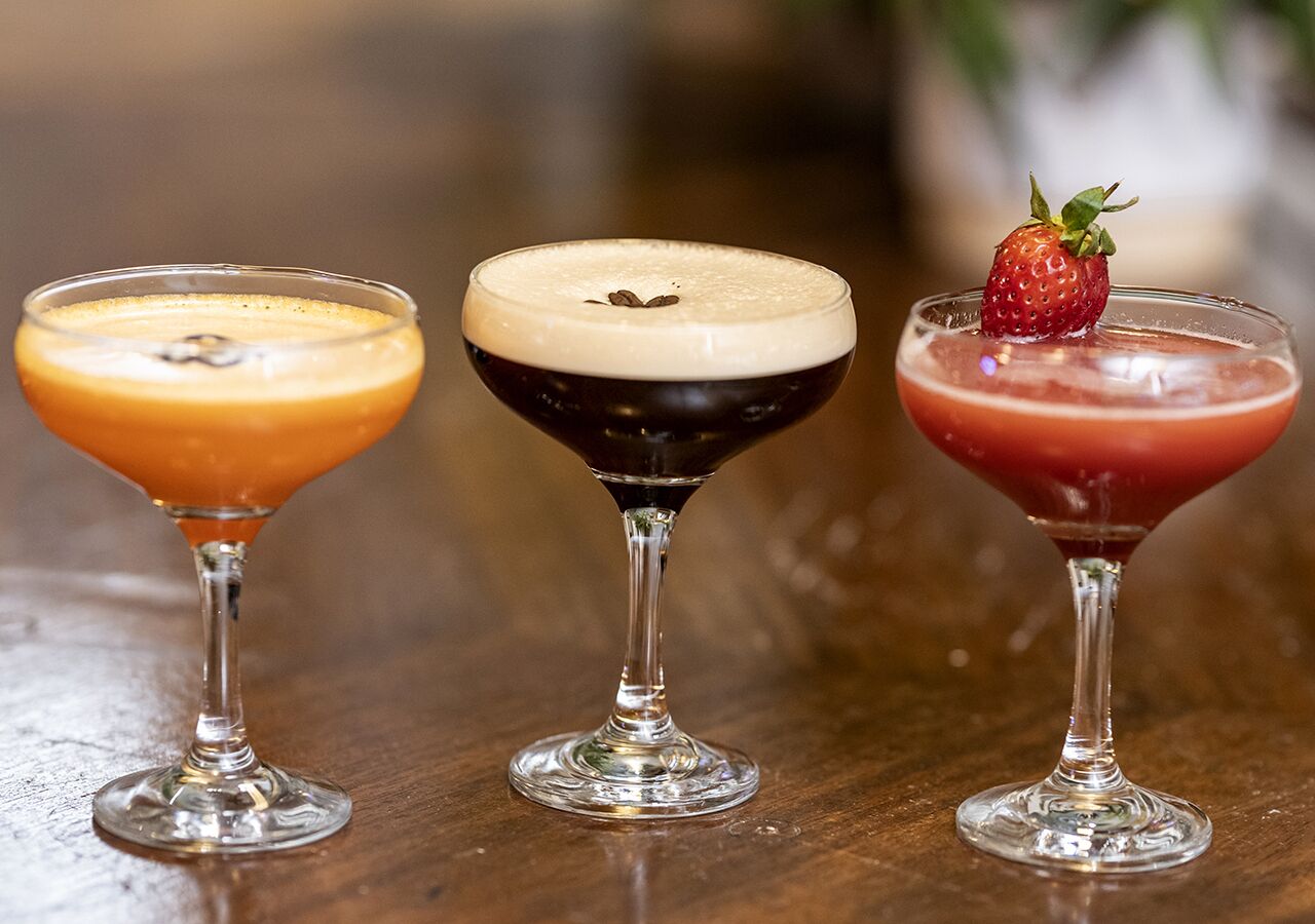 Drei Cocktails in Martini-Gläsern auf einer Holztischplatte.