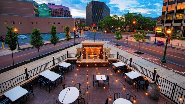 Un espace extérieur aménagé en terrasse, avec des tables et des chaises, une cheminée en briques et une vue sur le paysage urbain.