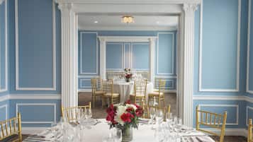 A formal dining room with a white table set for a meal, gold chairs, and a floral centerpiece.