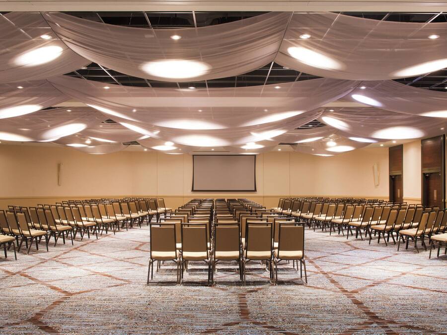 A conference room with rows of chairs facing a projection screen, a carpeted floor, and draped fabric on the ceiling.