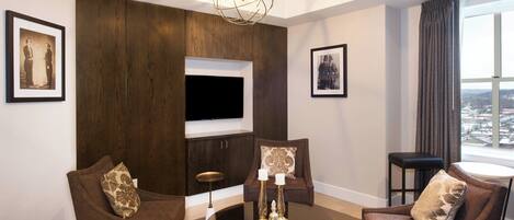 Una sala de estar moderna con una mesa de centro redonda de vidrio, dos sillones marrones, un sofá y un televisor montado en una pared de madera.