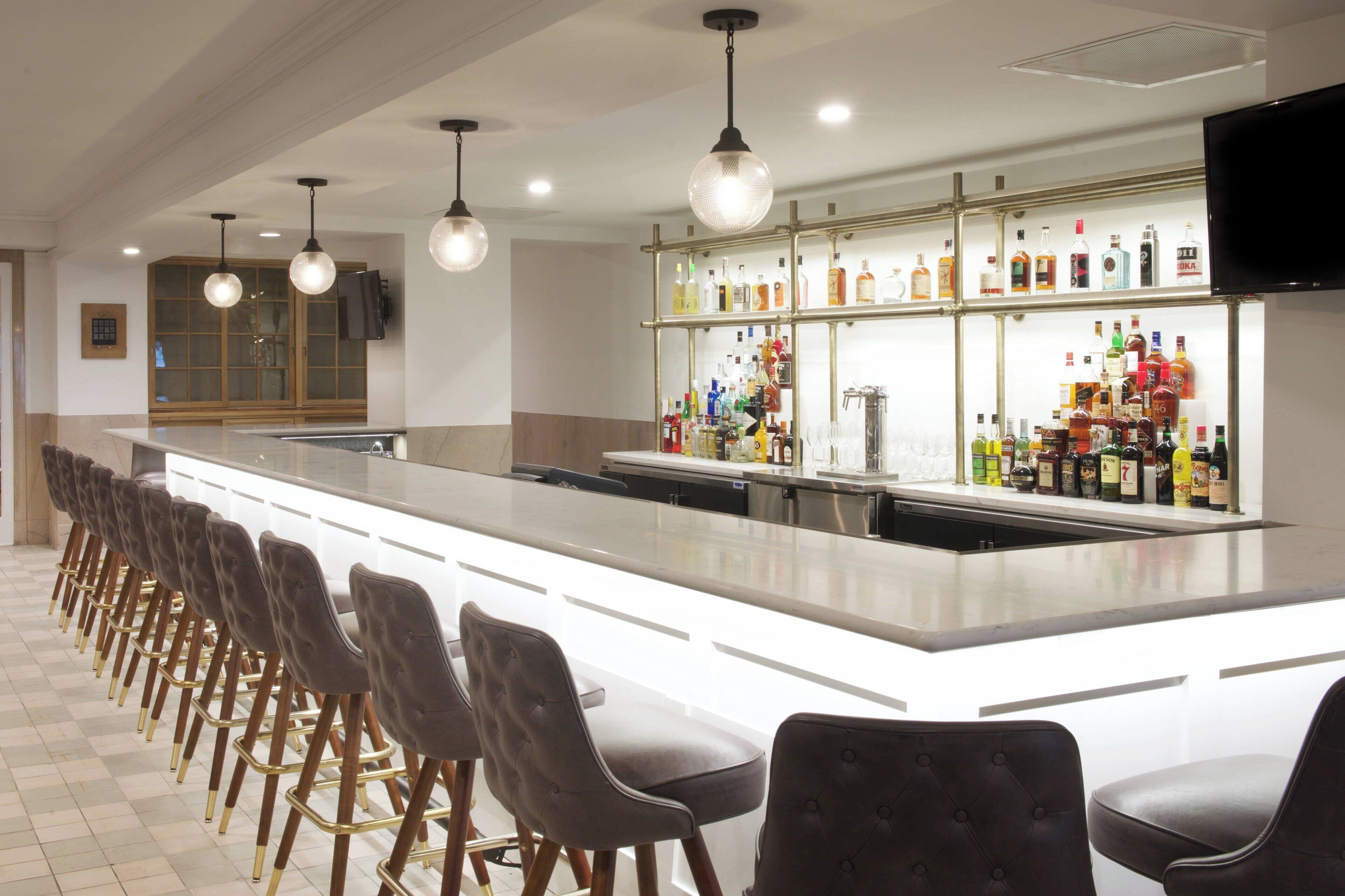 A bar area with a long counter, multiple stools, and a variety of liquor bottles on shelves.