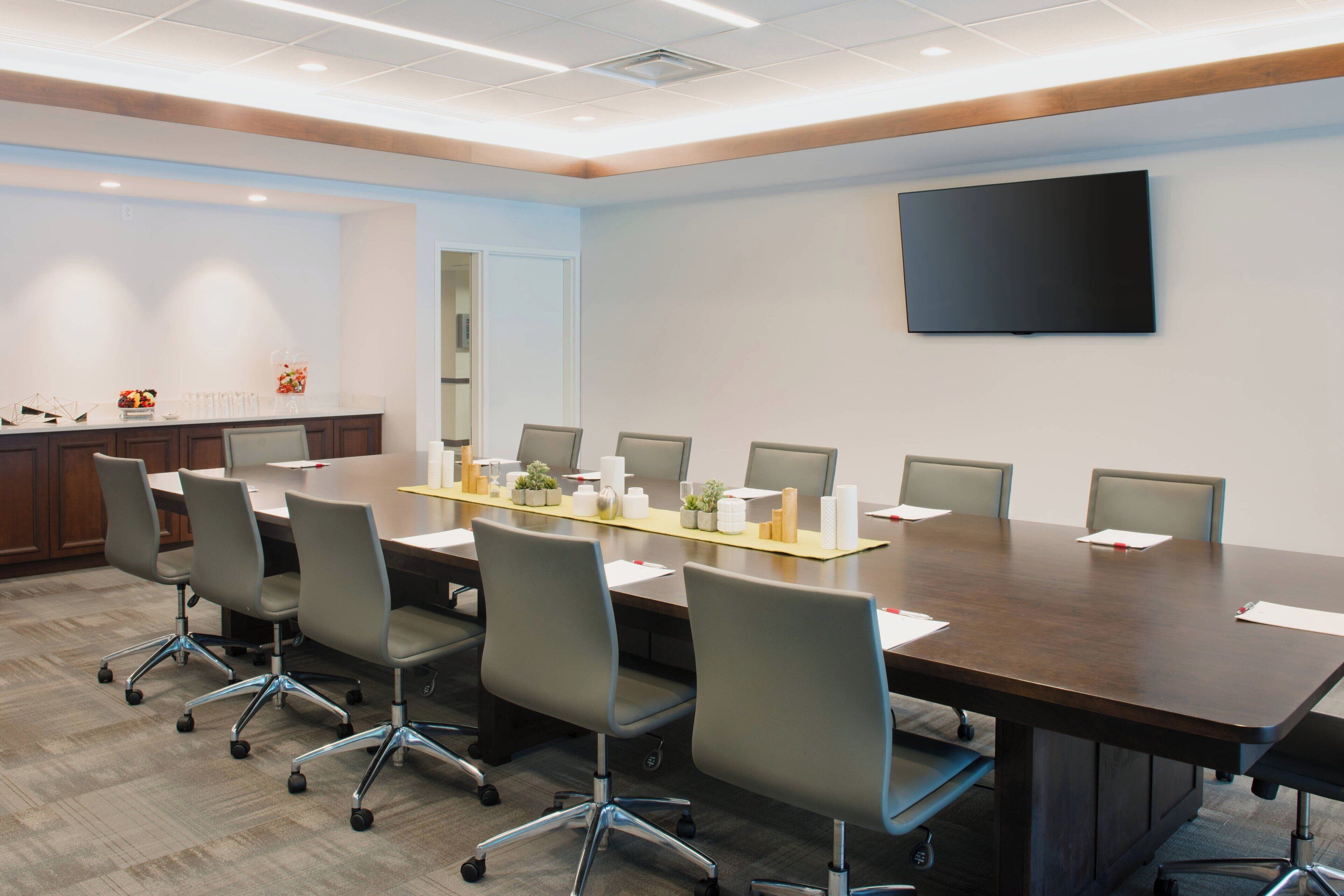 A conference room with a long table, six chairs, and a flat-screen TV on the wall.