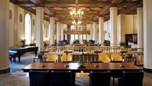 Un vaste hall doté d’un plafond haut, de colonnes richement décorées et d’un lustre. On y trouve de nombreuses tables et chaises disposées pour les repas ou les réunions.