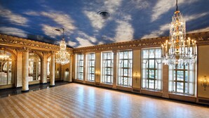 Une salle de bal spacieuse, dotée de grandes fenêtres, de lustres somptueux et d’une architecture classique.