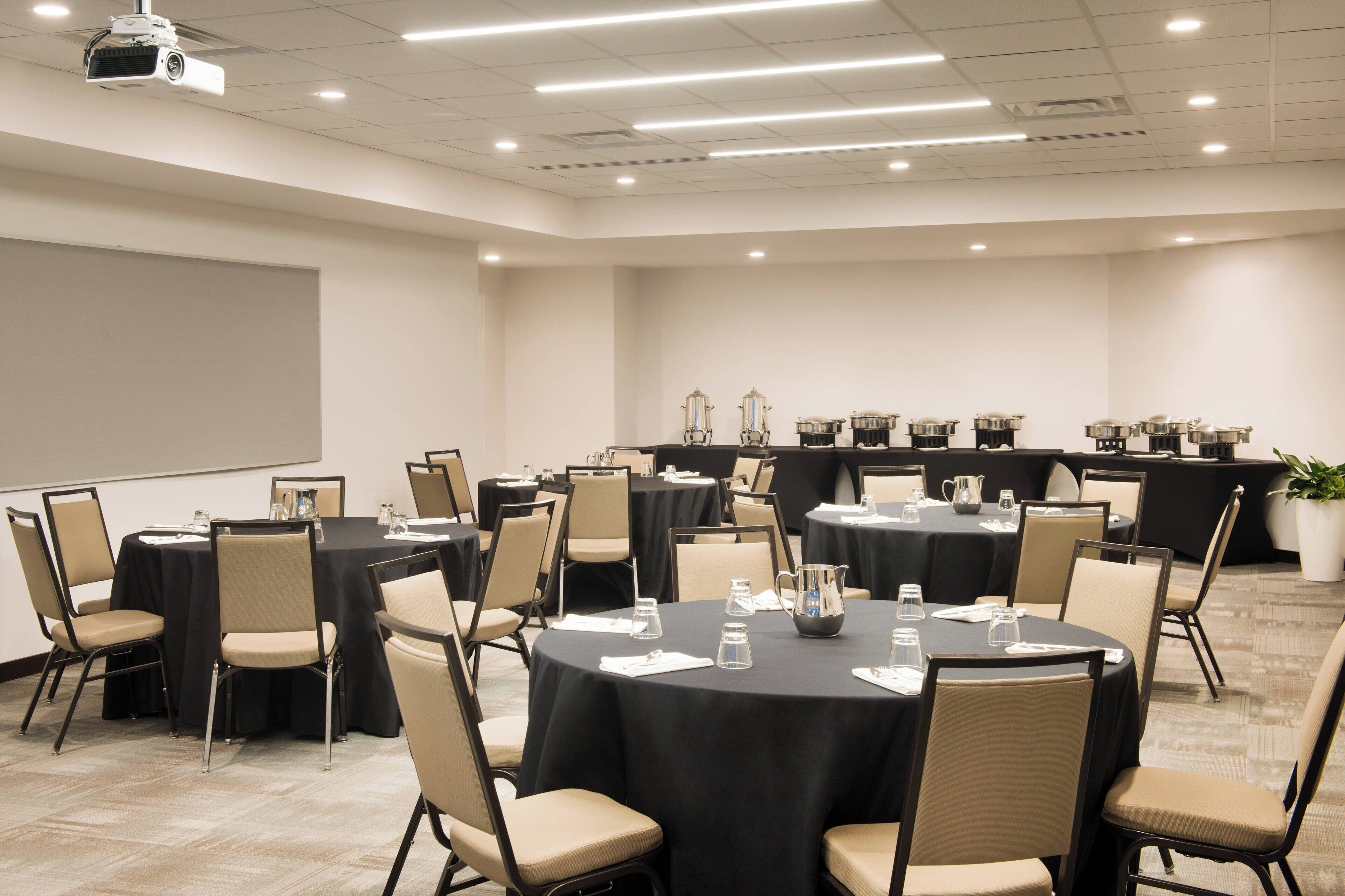 A conference room with multiple round tables, chairs, and a projector screen.