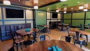 A restaurant with wooden tables and chairs, a green wall, and a large flat-screen TV.