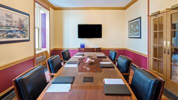 Un salón de conferencias con una larga mesa, sillas de cuero negro, un televisor de pantalla plana y obras de arte enmarcadas en las paredes.