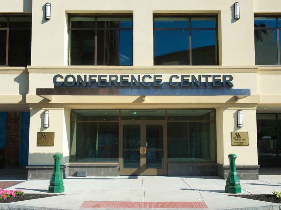 The exterior of a conference center with a large entrance, glass doors, and a sign above the doors.