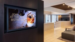 A modern lobby with a large digital screen advertising a new bistro bar, a seating area with a sofa, and a staircase leading to another level. - Courtyard by Marriott - Atlanta Executive Park/Emory (Atlanta)
