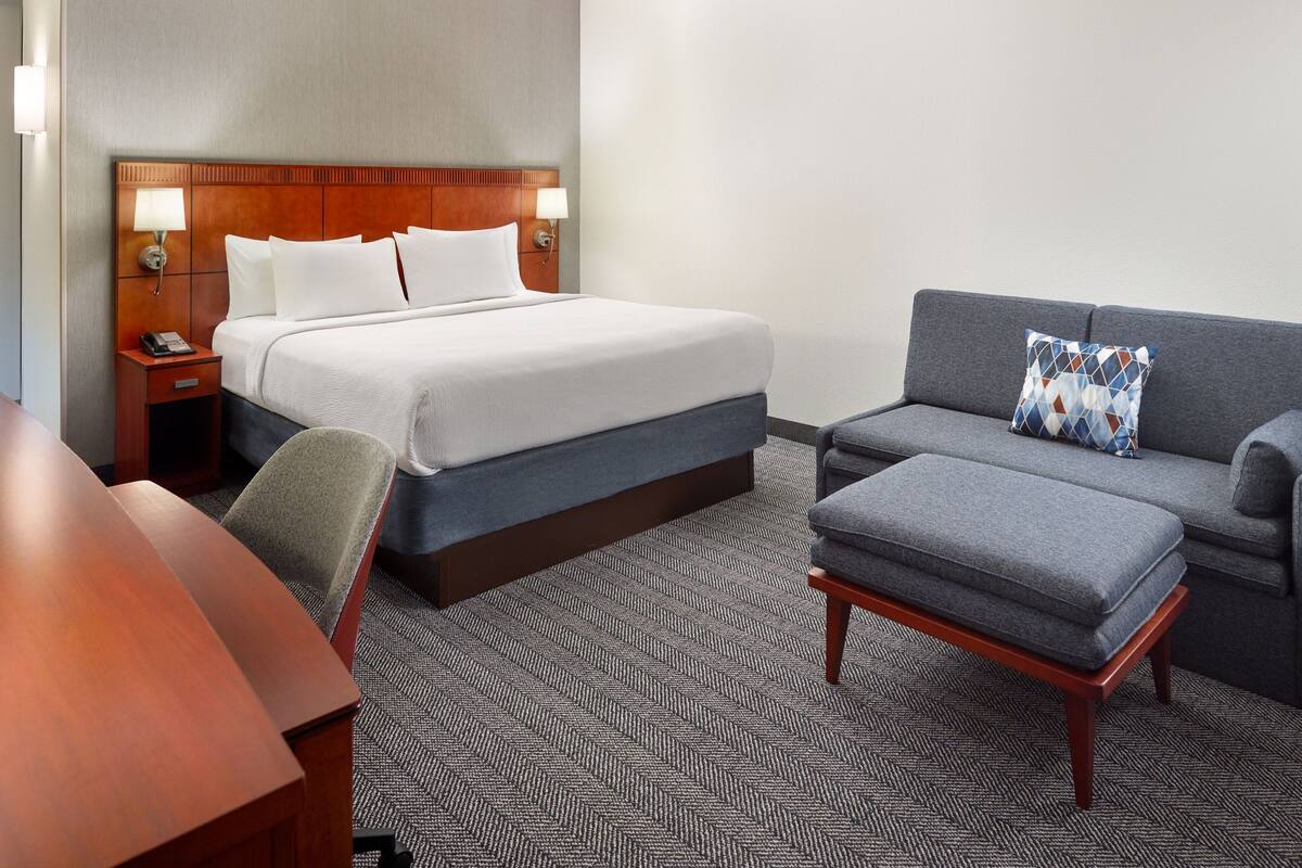 Una habitación de hotel con una cama grande, un sofá, una mesita y una silla.