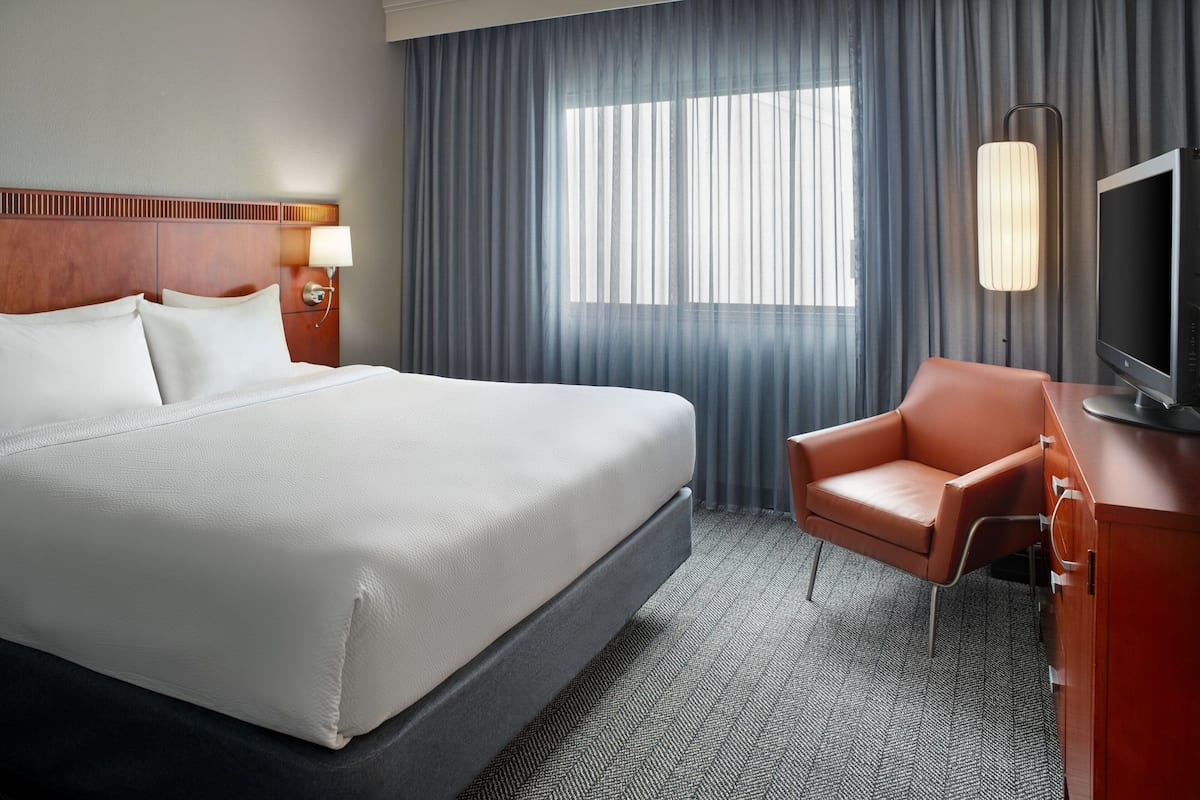 Habitación de hotel con una cama grande, un sillón de cuero, un televisor y una ventana con cortinas.