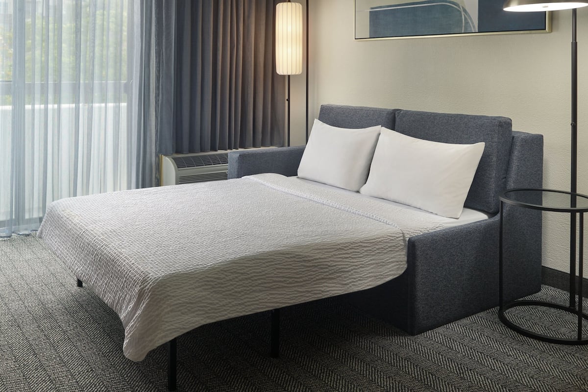 Una habitación de hotel con una cama, una lámpara de pie y un ventanal con cortinas.