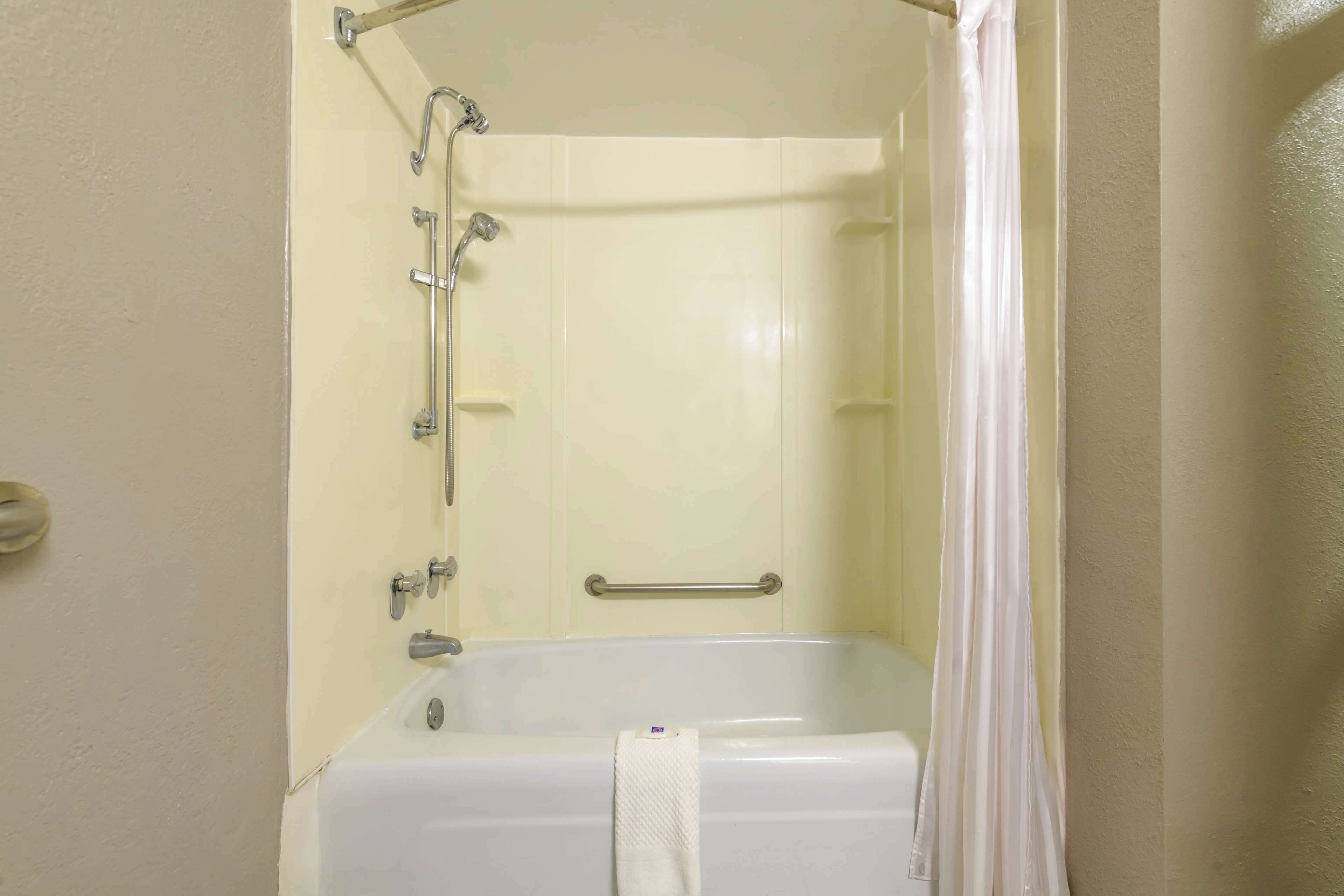 Una bañera blanca estándar con cortina de ducha, barras de apoyo y un perchero.