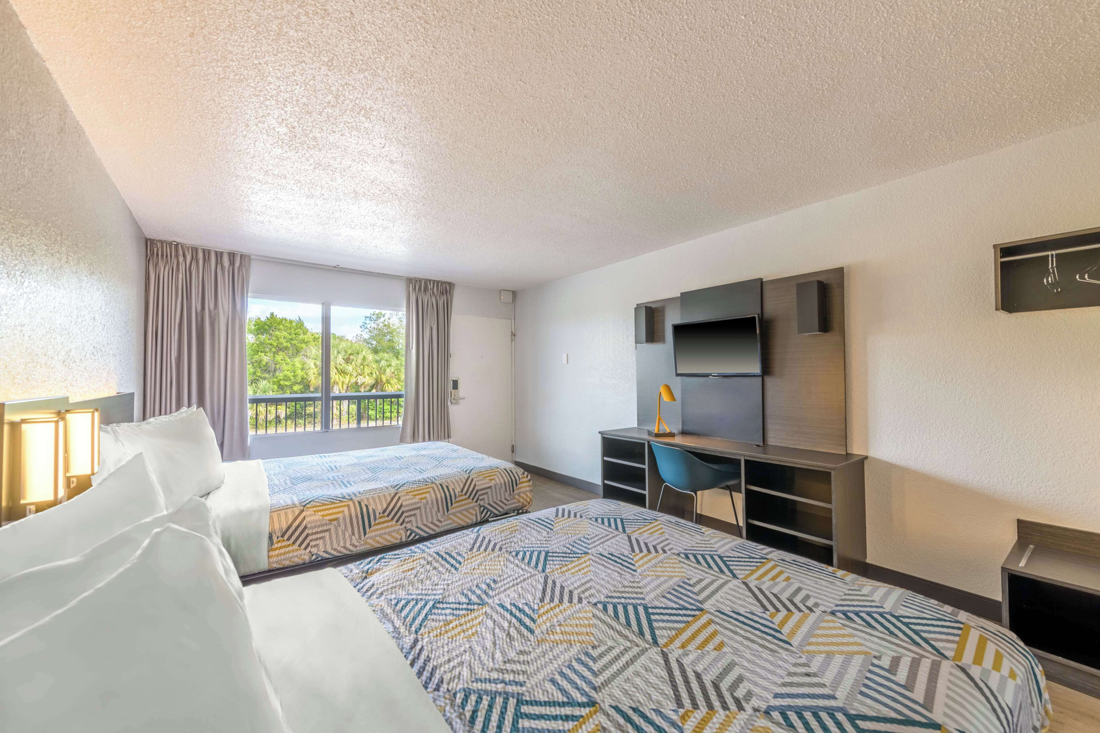 Habitación de hotel con dos camas, un escritorio, un televisor y un balcón con cortinas.