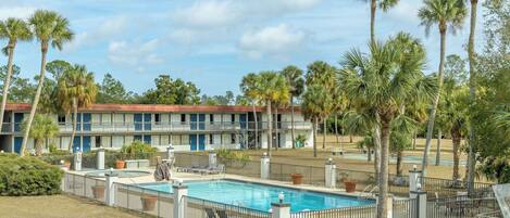 Un hotel con piscina, palmeras y una terraza delimitada por una valla.