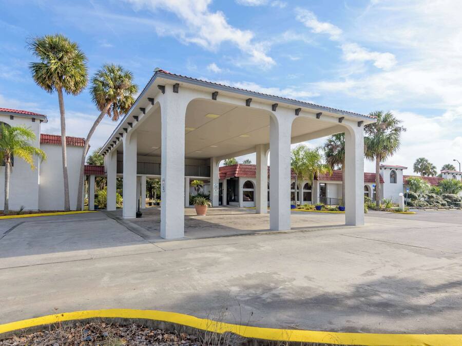A covered outdoor area with a white building, palm trees, and a clear sky.