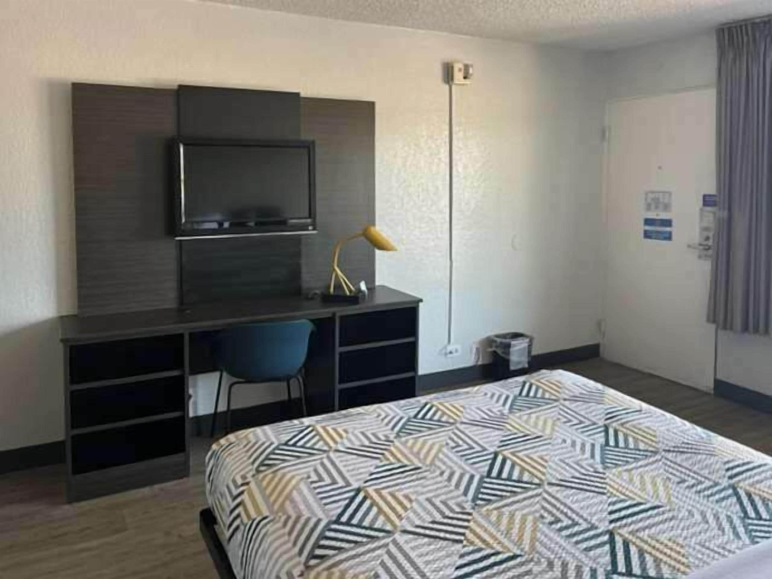Une chambre d’hôtel comprenant un lit, un bureau avec une chaise, une télévision et une lampe.