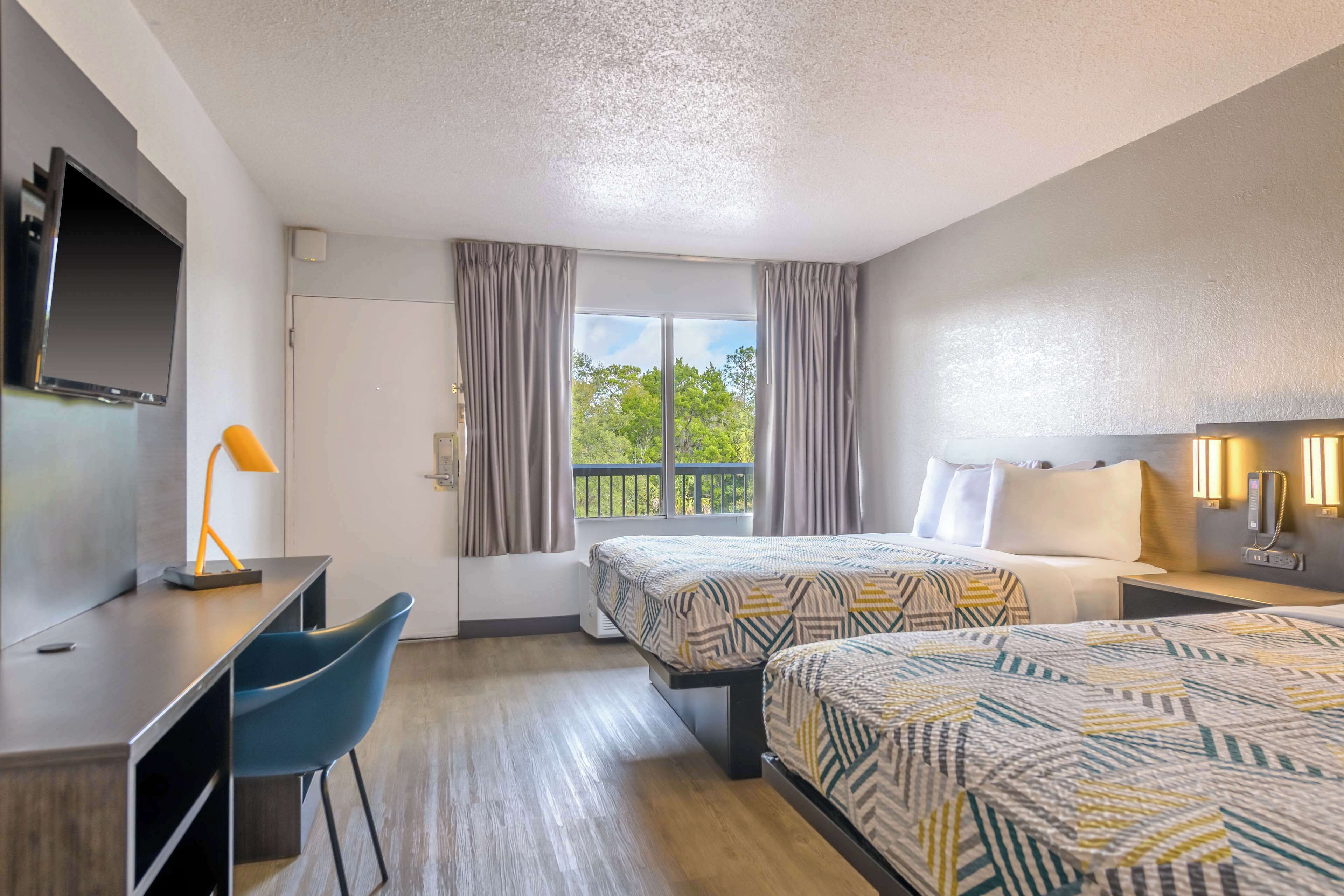 A hotel room with two beds, a desk, a chair, a TV, and a window with curtains.