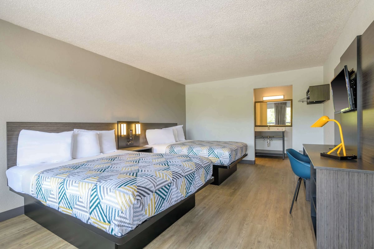 A hotel room with two beds, a desk, a chair, a TV, and a bathroom.