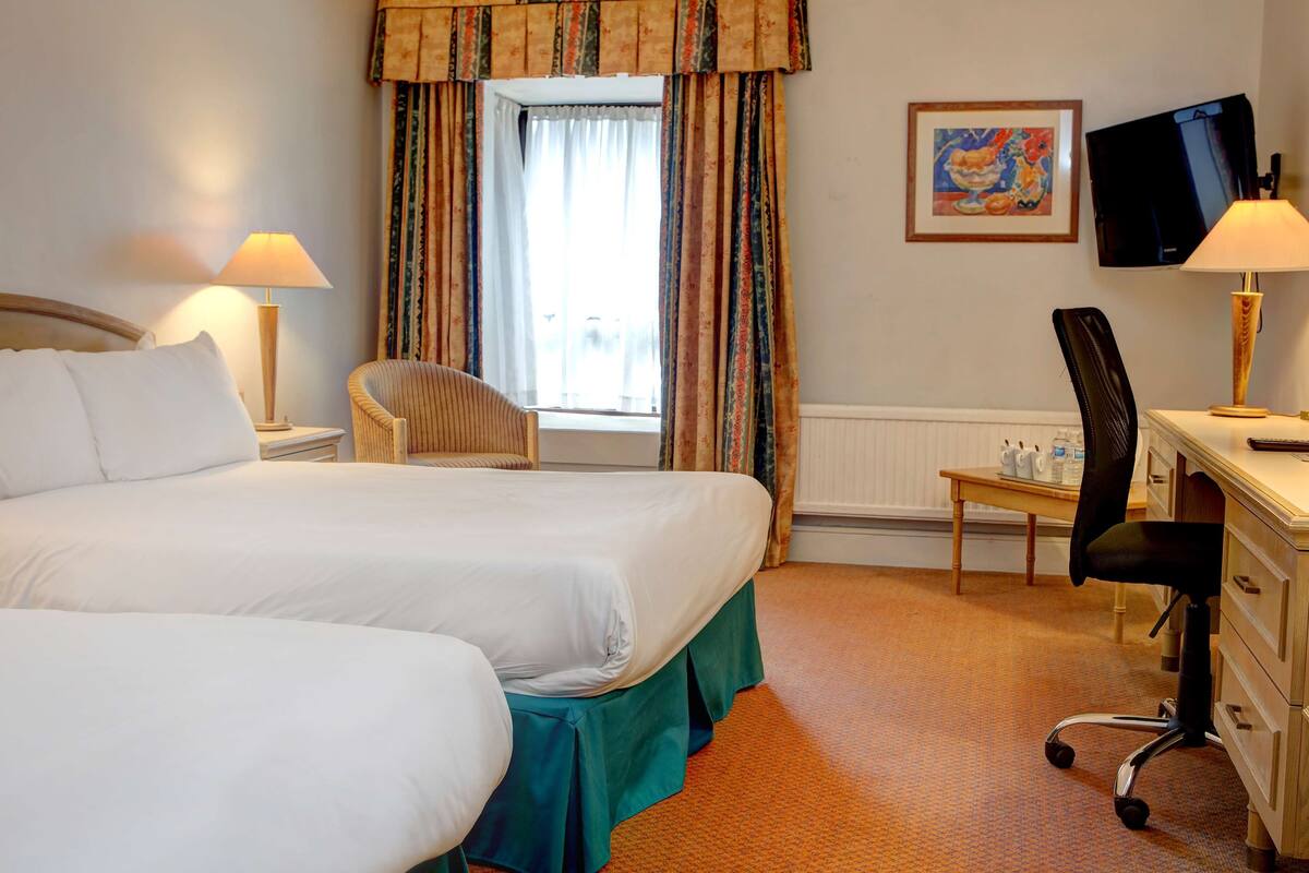 A hotel room with two beds, a desk, a chair, a television, and a window with curtains.