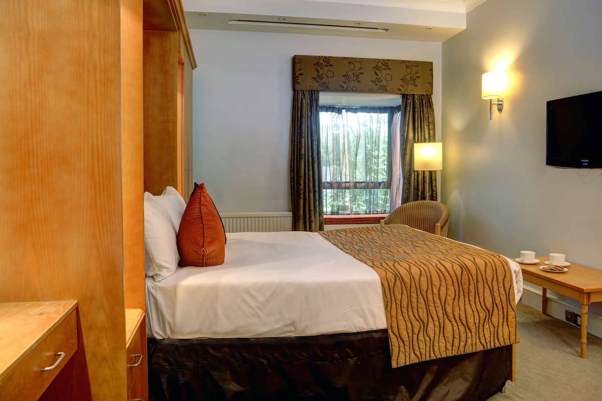 A hotel room with a bed, a desk, a chair, a TV, and a window with curtains.
