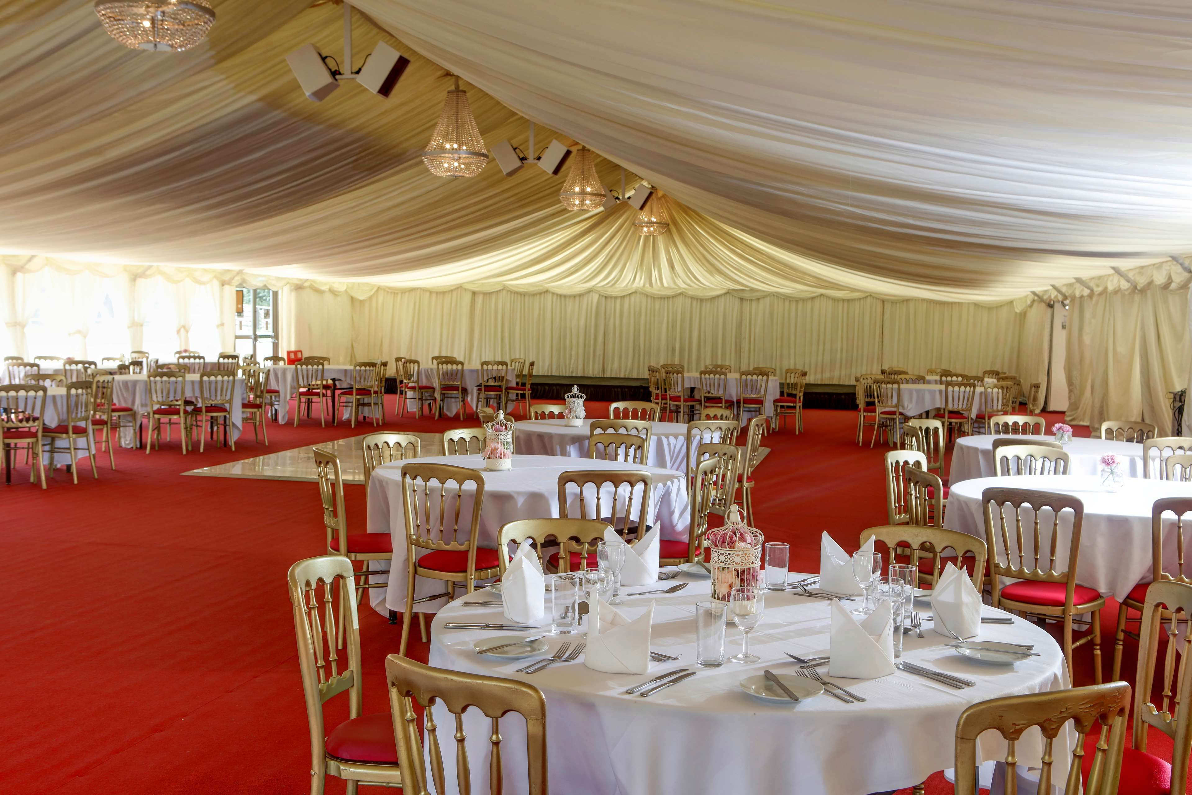 Un salón de banquetes con mesas redondas, manteles blancos y sillas rojas.