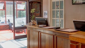 Una mesa de recepción con una computadora, una planta en maceta y un área de estar con un sofá y sillones.